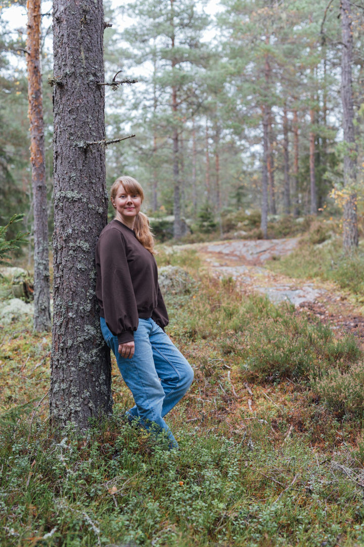 nainen nojaa metsässä selkä männyn runkoa vasten